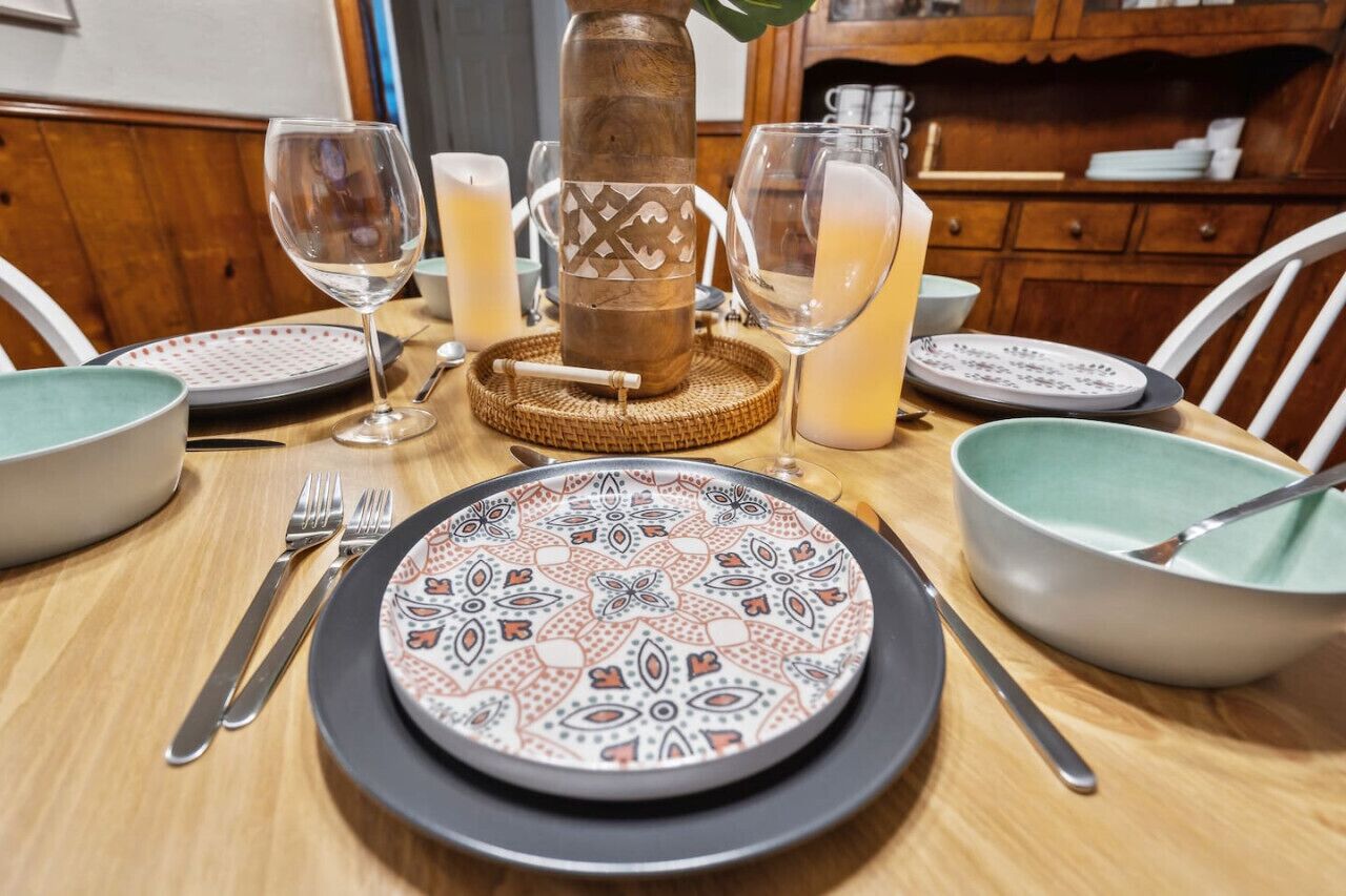 Une table à manger dressée avec des assiettes à motifs, des couverts et des bougies, agrémentée d’un centre de table décoratif.