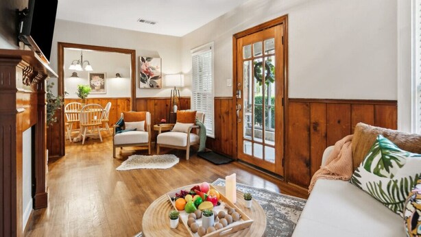 A cozy living room with wooden floors, a dining area with a wooden table and chairs, and a large window with a wreath decoration. - This is Your Home Away From Home! Warm & Comfy 2BD (Fort Worth)