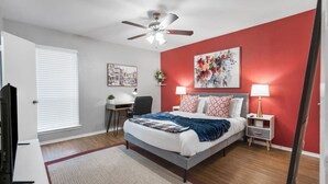 A bedroom with a bed, bedside tables, a desk, a chair, a ceiling fan, and artwork on the walls. - Homey 1BD: TCU Walkable, Cozy & FUN-filled! (Fort Worth)