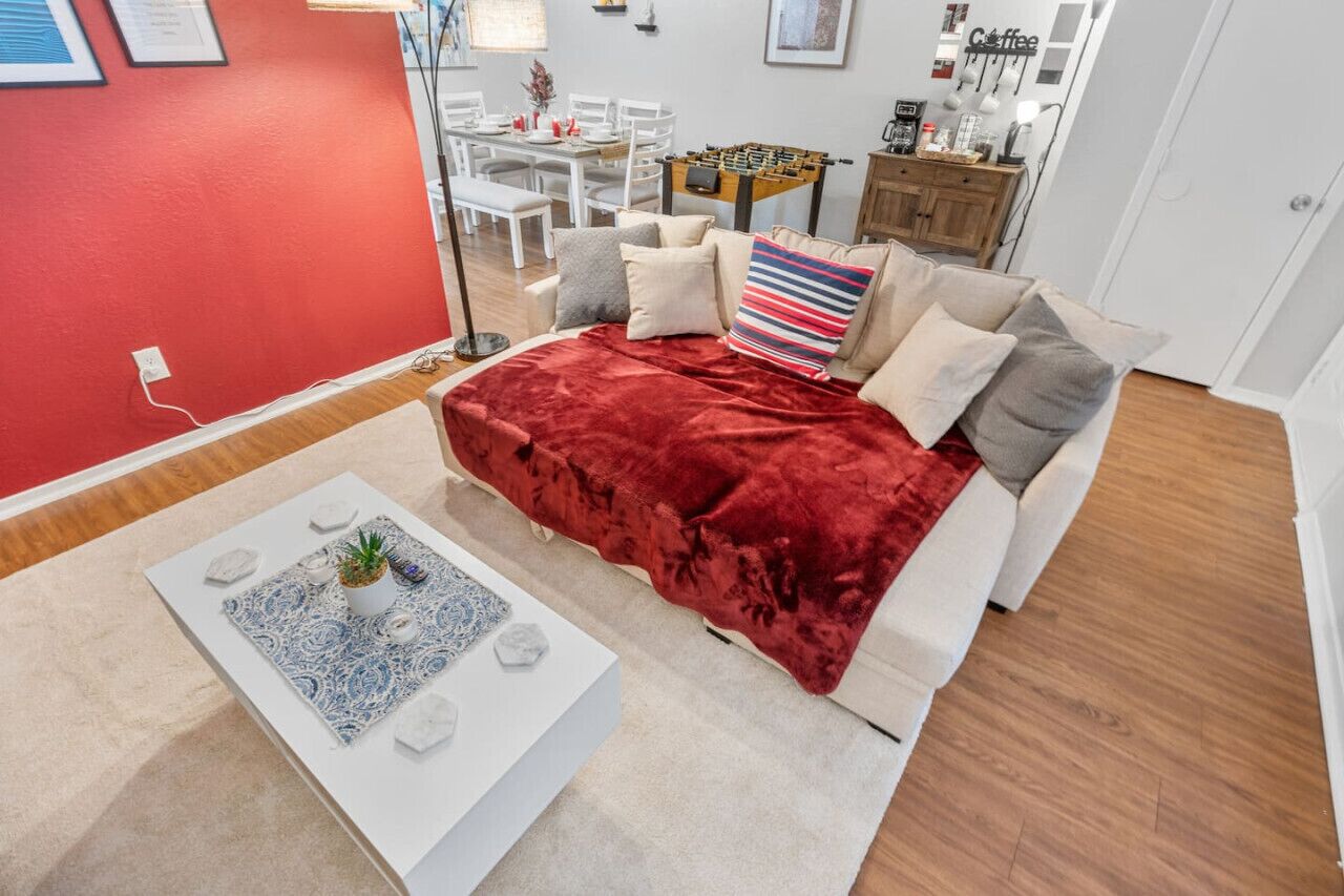 A modern living room with a red velvet sofa, a white coffee table with decorative items, and a dining area in the background.