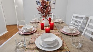 A dining table set with white plates, bowls, and wine glasses, surrounded by red candles and a decorative centerpiece. - Homey 1BD: TCU Walkable, Cozy & FUN-filled! (Fort Worth)