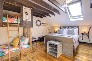 A bedroom with a loft bed, a ladder, a small bench, a wooden chest, a round mirror, and a window with a view.
