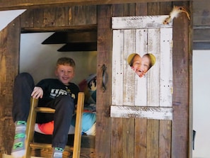 A child sitting on a wooden ladder in a rustic room with a heart-shaped cutout in the wall.