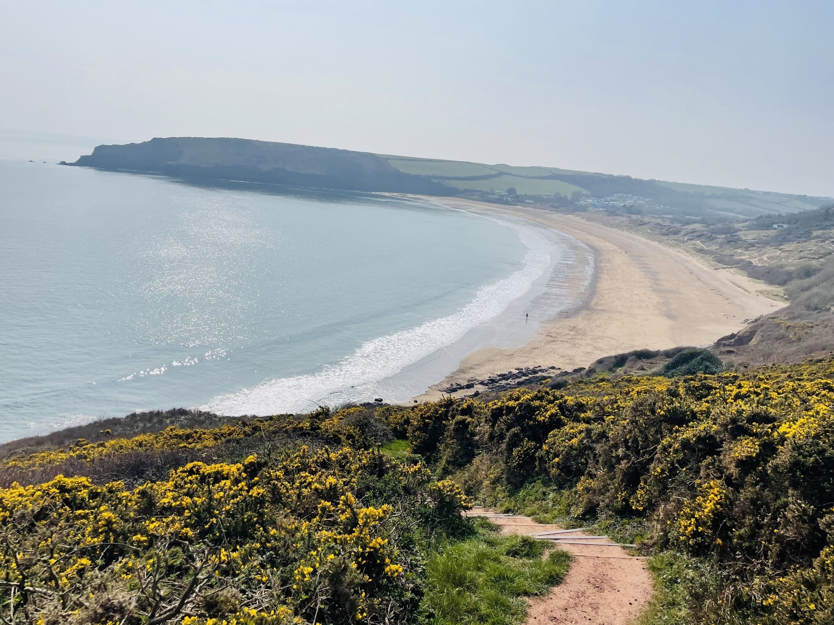 Eine Küstenlandschaft mit sandigem Strand, blauem Himmel und einem Weg zum Strand.