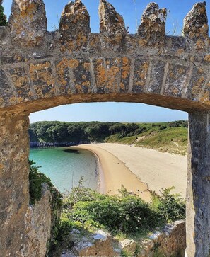 A stone archway framing a beach with clear water and greenery in the background.
