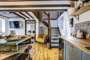 Une cuisine rustique avec des poutres en bois, un escalier en bois et un coin repas où une table est dressée pour le repas.