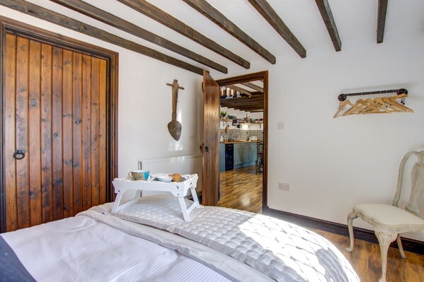 A bedroom with a wooden door, a bed with a white headboard, a wooden chair, and a wooden ceiling with exposed beams.