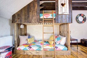 Ein Stockbett mit Holzleiter, eine gesteppte Bettdecke und ein kleiner Tisch mit Stuhl.