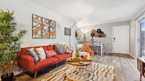 Una sala de estar con un sofá rojo, una mesa de centro con frutas, una lámpara y un comedor con una mesa y sillas blancas.