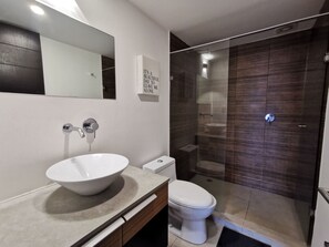 Un baño moderno con un lavamanos blanco grande, un inodoro y una ducha con mampara de vidrio.
