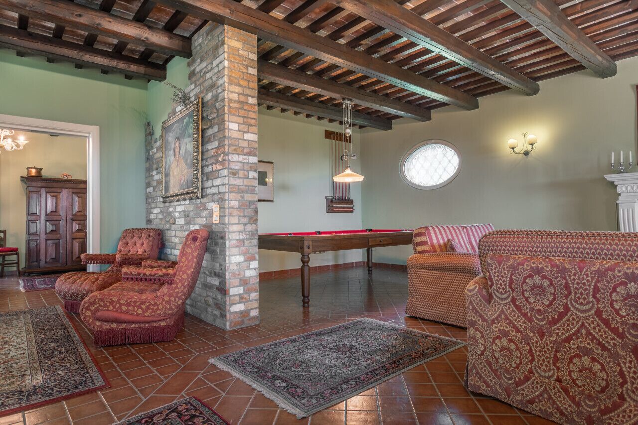 A room with a pool table, two armchairs, a sofa, and a brick column.