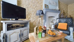A living room with a television on a white cabinet, a fireplace, a leather armchair, and a coffee table with pastries and a vase.