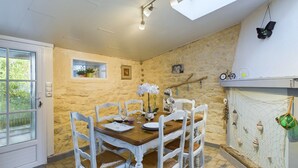 A dining area with a stone wall, white chairs, a wooden table, and a window with a view of greenery.