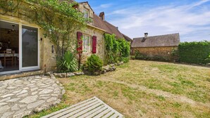 A stone house with a garden, a wooden deck, and a stone pathway leading to the entrance. - Dordogne - Beautiful cottage for 8 with a pool (Saint Rabier)