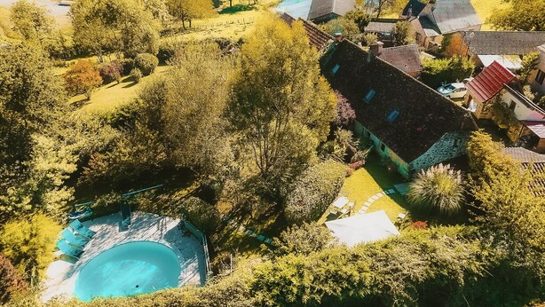 An aerial view of a residential area with a swimming pool surrounded by trees and a traditional building with a tiled roof. - Dordogne - Beautiful cottage for 8 with a pool (Saint Rabier)