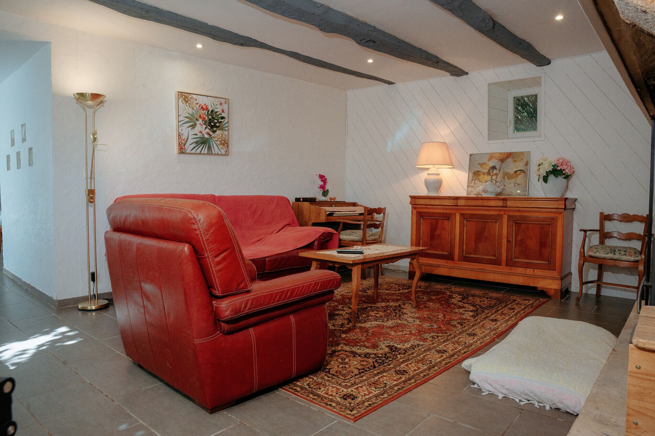 A living room with a red leather sofa, a wooden cabinet, and a floor lamp.
