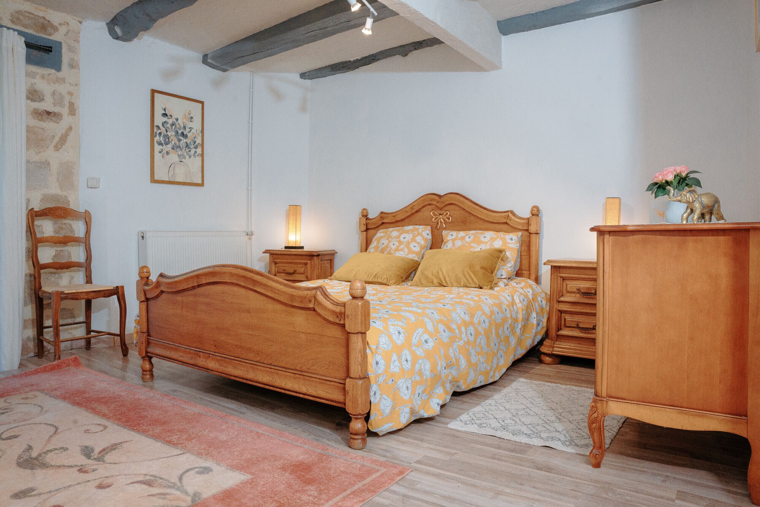 Ein Schlafzimmer mit einem hölzernen Bett, Nachttischen, einem Sessel und einer Kommode.