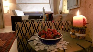 A cozy living room with a patterned sofa, a small table with a bowl of strawberries, and a lit candle. - Double Room with Spa Bath (Uchisar)