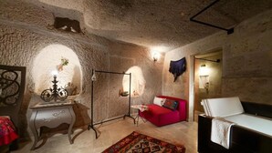 A room with a stone wall, a red sofa, a white sofa, a floor lamp, and a table with decorative items. - Double Room with Spa Bath (Uchisar)