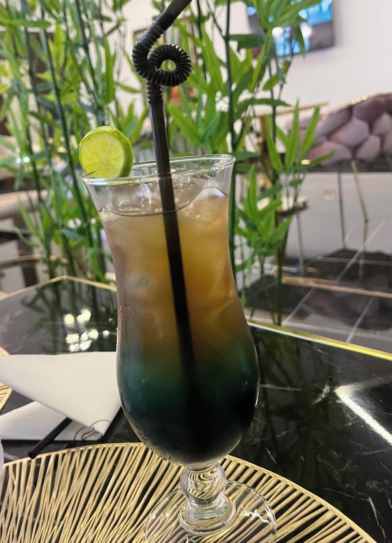 Ein Cocktail mit Limettenscheibe und schwarzem Strohhalm in einem Glas auf einem Tisch.