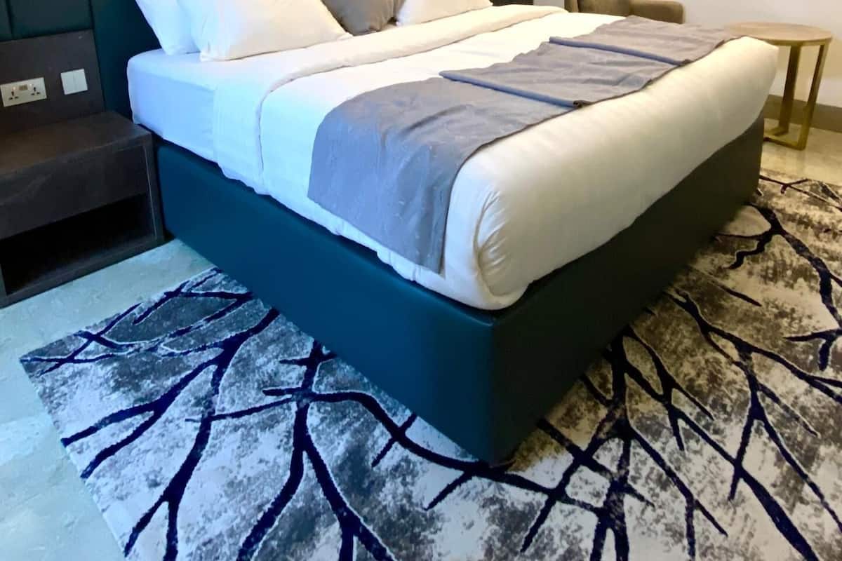 A modern hotel room with a large bed, a small side table, a chair, and a round table.