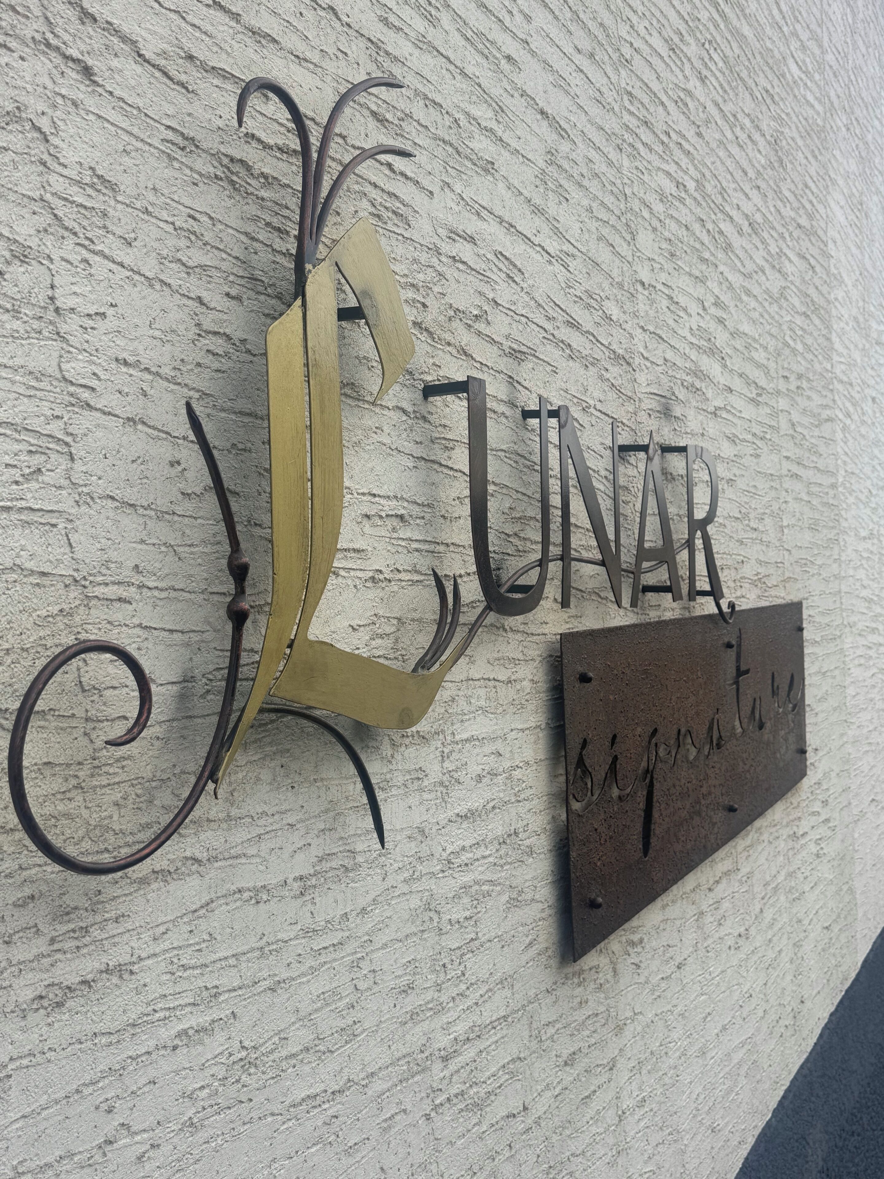 Une enseigne fixée au mur, portant le mot « LUNAR », et une plus petite enseigne en dessous, sur laquelle on peut lire « signature ».