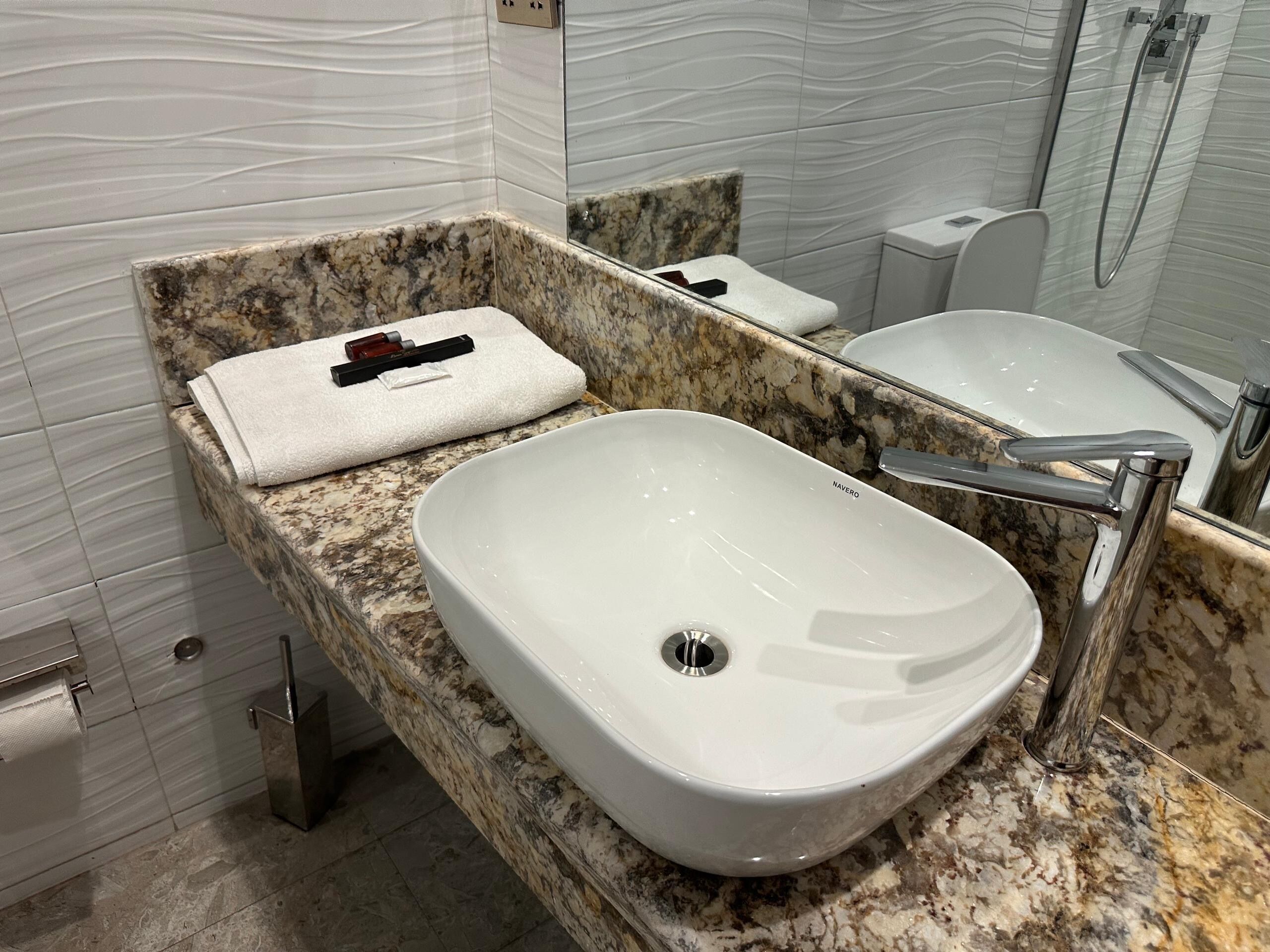 A bathroom with a white sink, a marble countertop, a towel, and a mirror.
