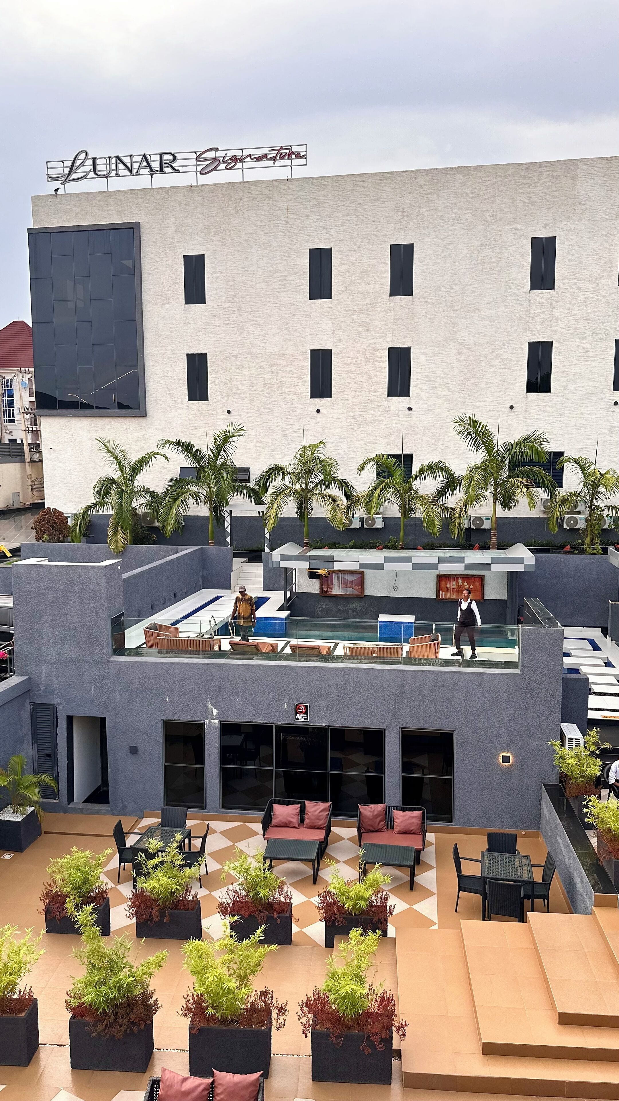 A rooftop lounge with outdoor seating, palm trees, and a sign reading "Lunar Signature".