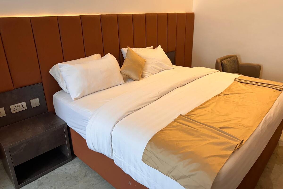 A neatly made bed with white and beige bedding, a wooden headboard, and a nightstand with a drawer.