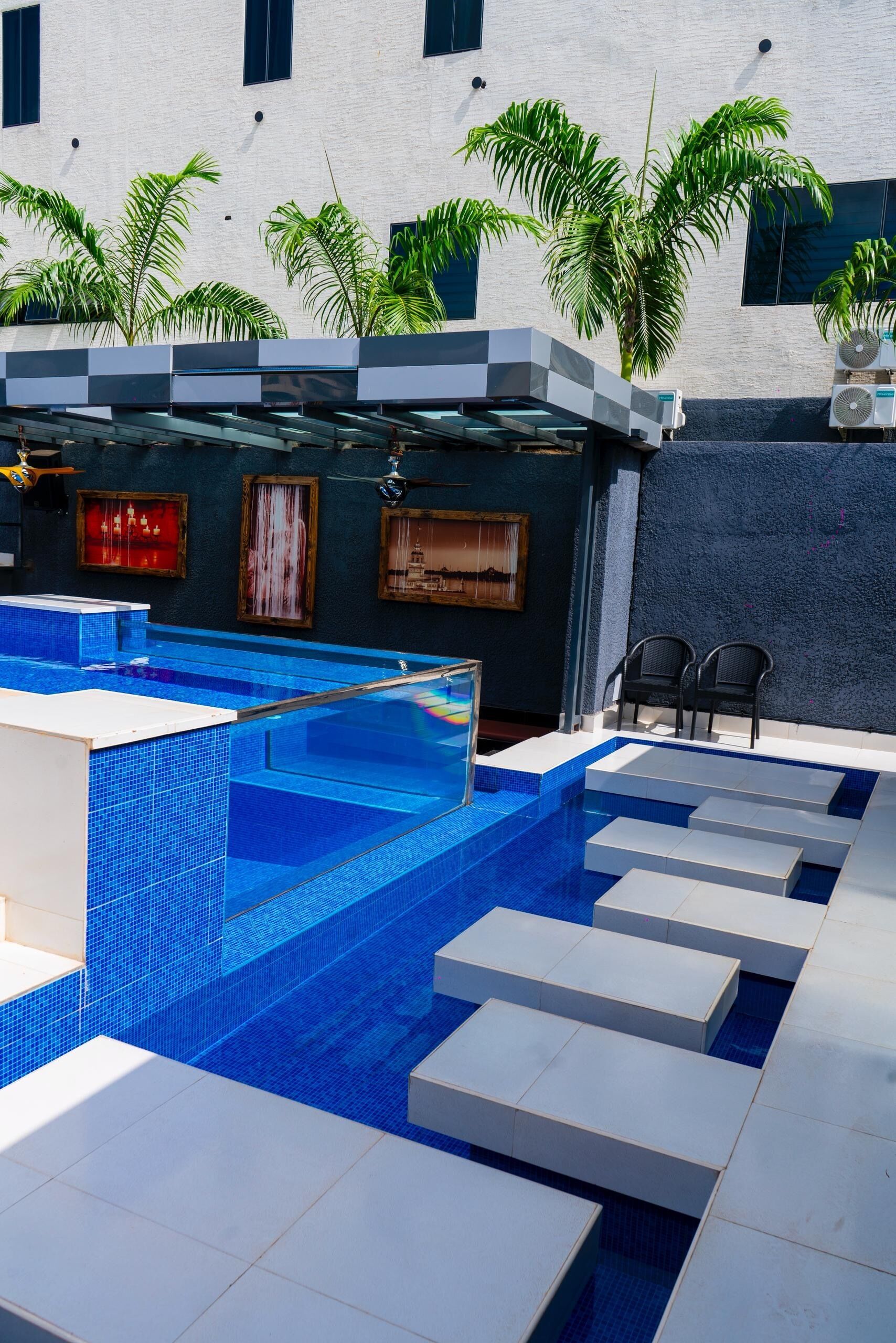 A modern pool area with blue-tiled steps leading into the pool, surrounded by palm trees and a building with large windows.