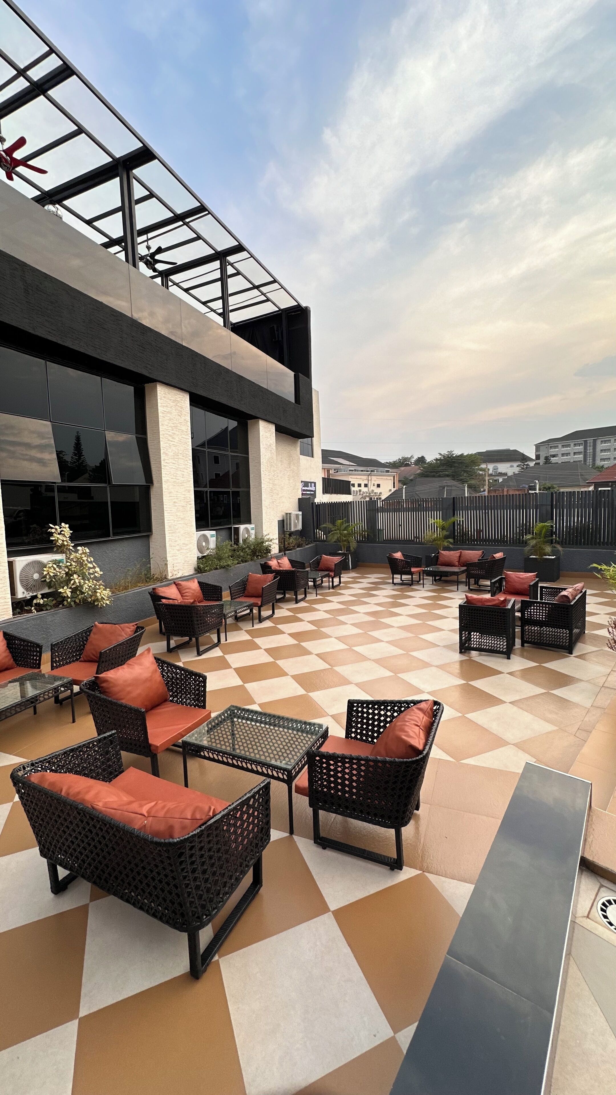An outdoor seating area with checkered flooring, wicker furniture, and a glass ceiling structure.