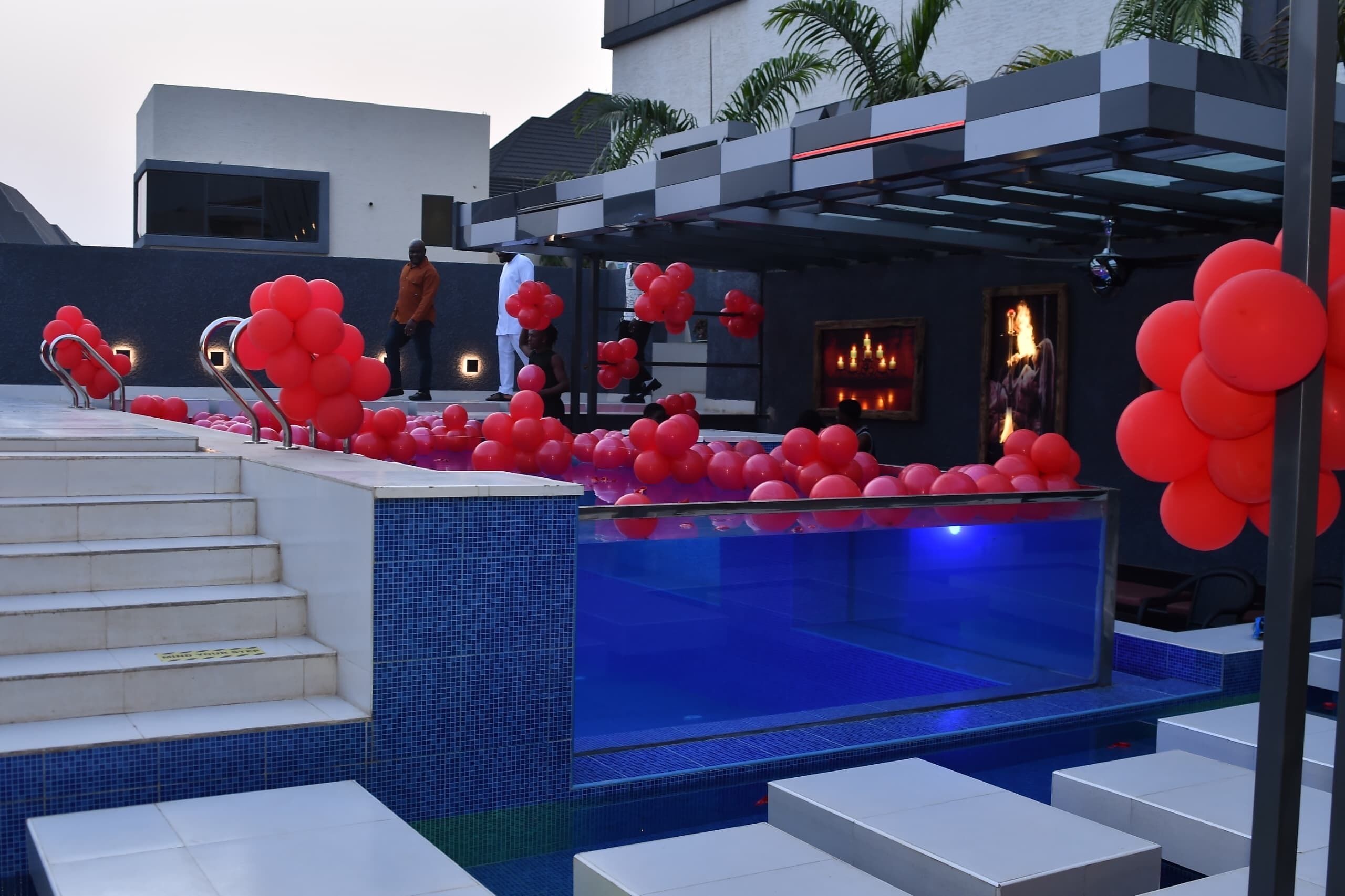 A pool area with red balloons, a glass enclosure, and steps leading to a covered seating area.