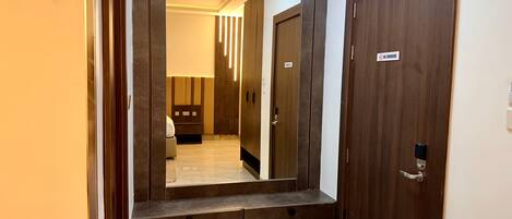 A hallway with a large mirror, a wooden door with a 'No Smoking' sign, and a bench.