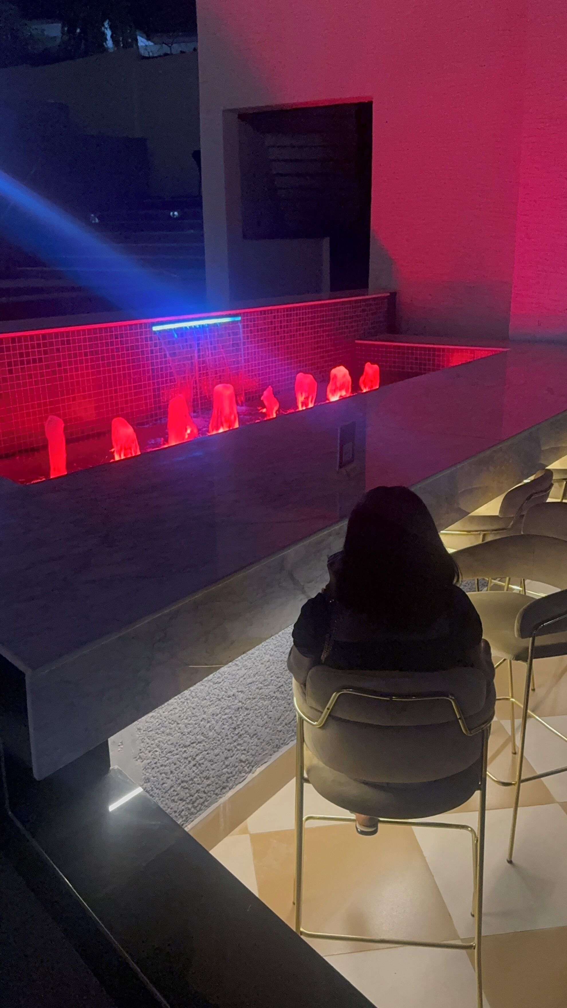 Uma área de bar com um recurso de água iluminado em vermelho e banquetas.