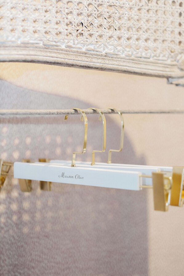 Een witte metalen standaard met een bordje waarop 'Maison Olive' staat en een goudkleurige kapstok.