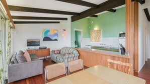 A modern living room with a sofa, a dining table, and a kitchen area with a green wall and wooden accents.