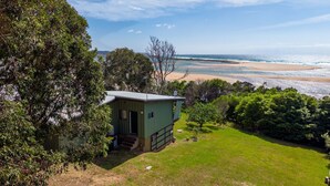 A small, single-story building with a flat roof, situated on a grassy area with a view of a beach and ocean.