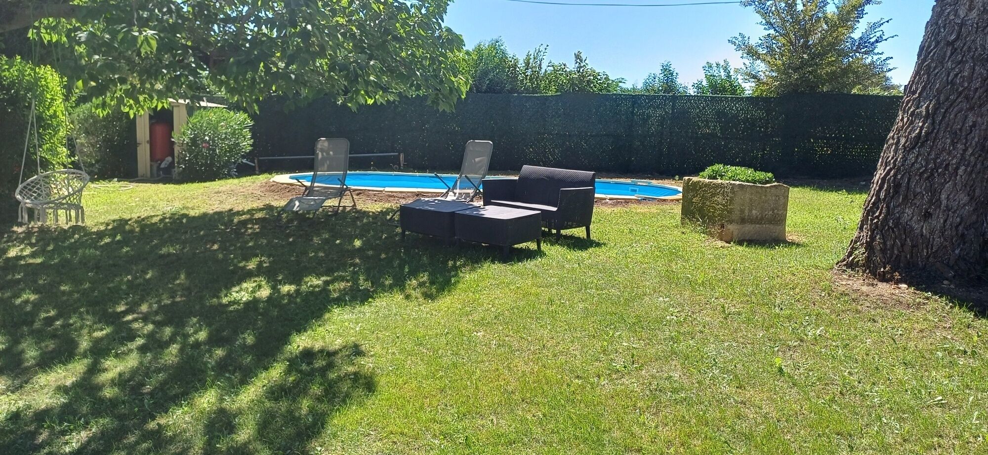 Un jardin avec une piscine, une balançoire et un espace détente comprenant une table et des chaises.