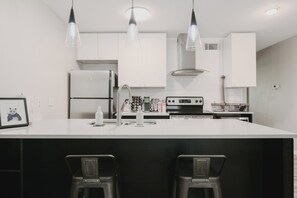 Una cocina moderna con armarios blancos, una isla central con taburetes altos e iluminación colgante.
