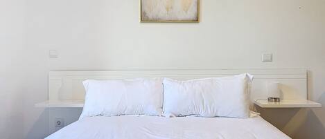 A neatly made bed with white bedding, a headboard, and two bedside tables with lamps.