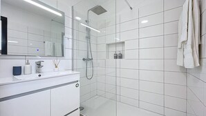 A modern bathroom with a glass shower enclosure, a white vanity with a mirror, and a towel hanging on the wall.