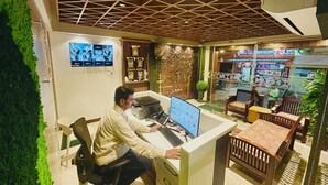 A man working at a desk with a computer, surrounded by wooden furniture and a decorative wall. - Eagle Stay Inn (Kanchipuram)