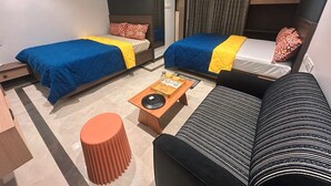 A hotel room with two beds, a sofa, a small table with a tray, and a red stool. - Eagle Stay Inn (Kanchipuram)