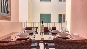 Una mesa de comedor con cuatro sillas, una botella y cristalería en un balcón con barandilla.