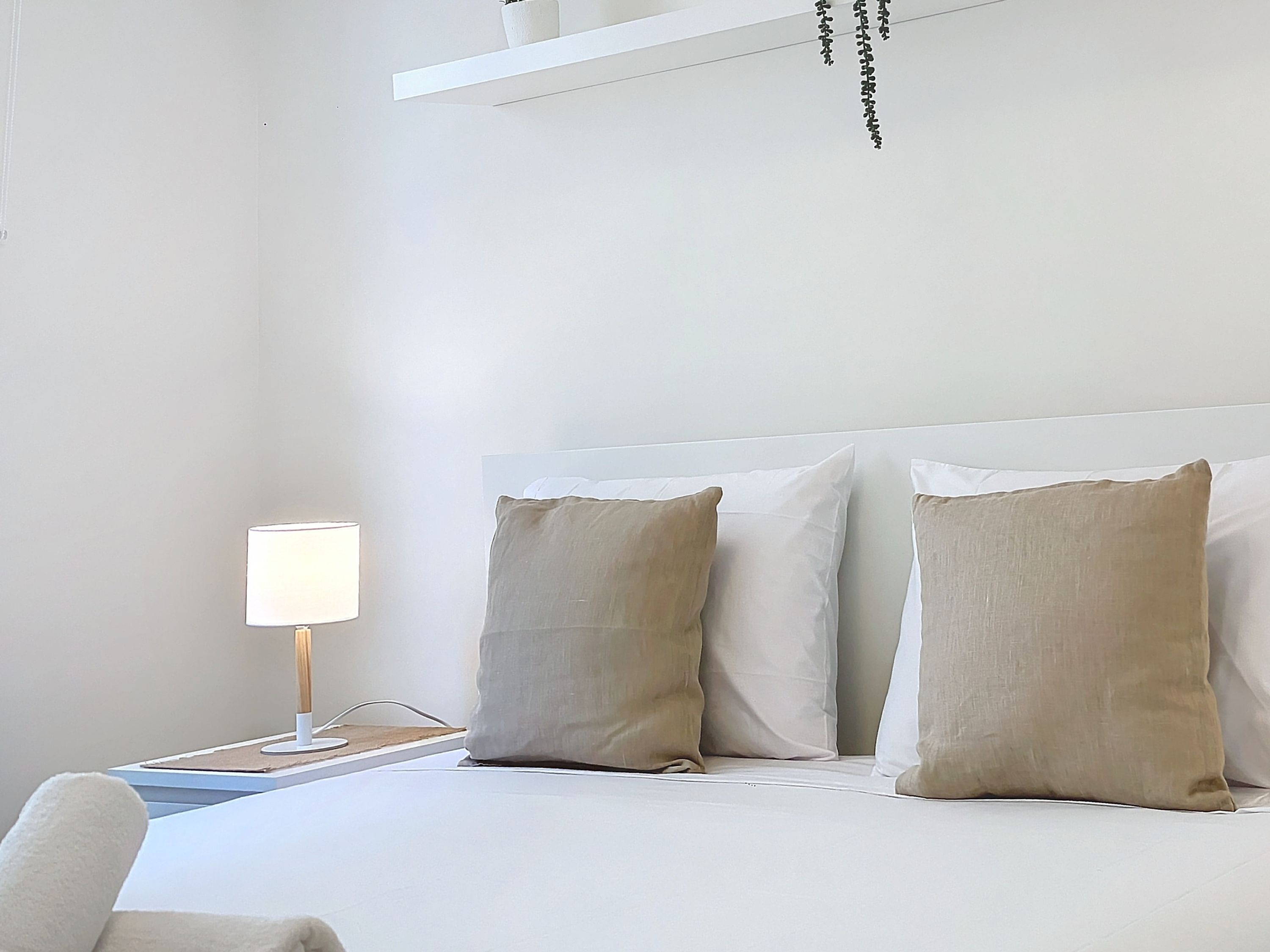 Een hotelkamer met een bed, twee kussens, een nachtkastje met een lamp en een witte muur.