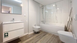 Un baño moderno con un espejo grande, un lavabo, una mesita de noche pequeña, un inodoro y una ducha con mampara de vidrio.