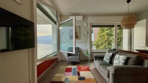 Ein modernes Wohnzimmer mit großem Fenster, einem grauen Sofa, einem farbenfrohen Teppich und einer hängenden Leuchte.