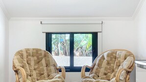 Deux fauteuils en osier assortis de coussins, un petit pouf et une fenêtre donnant sur un paysage verdoyant.