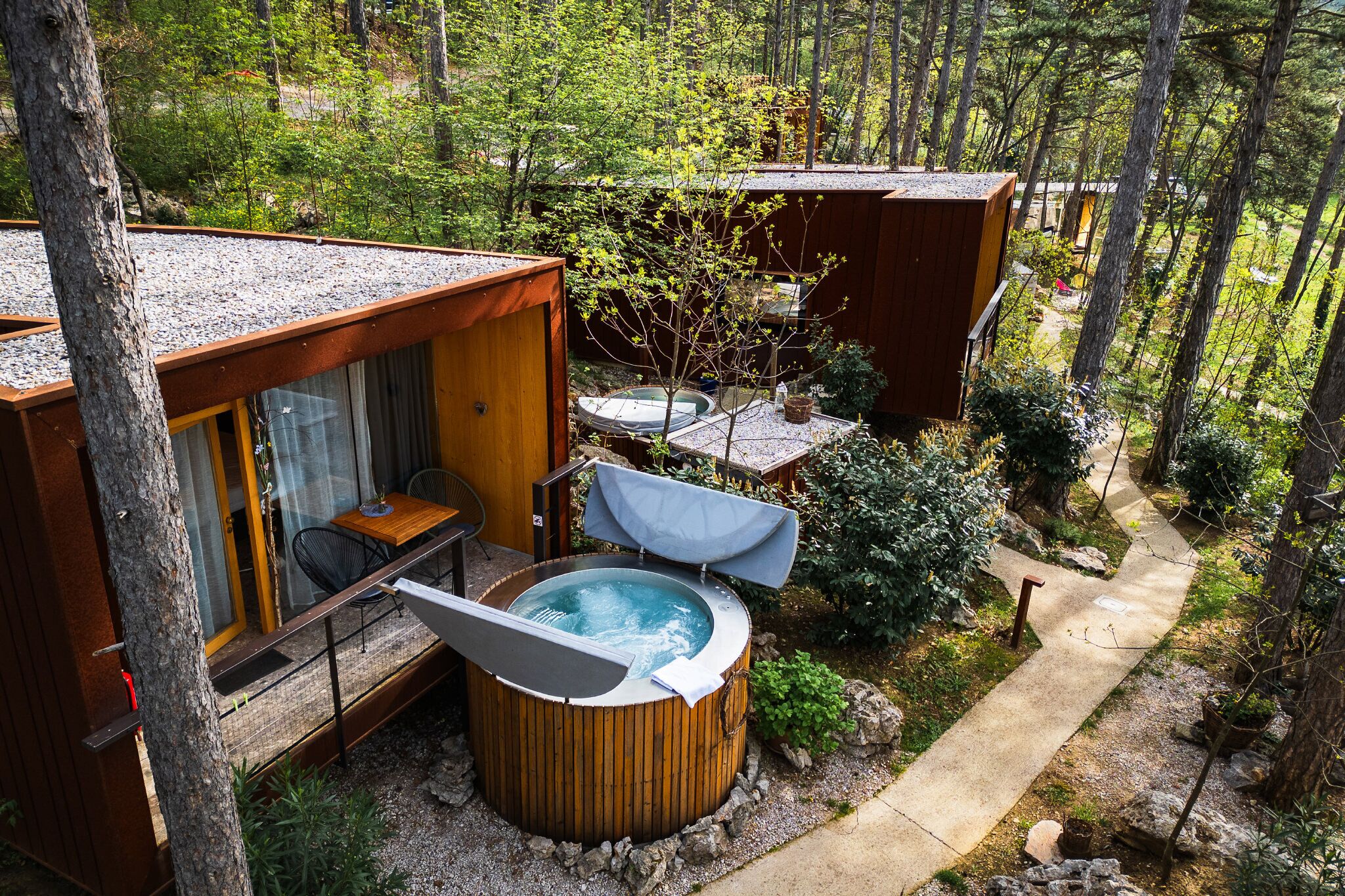 Una cabaña aislada con hidromasaje, terraza de madera y comedor rodeado de árboles.