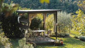A wooden deck with a table and chairs, surrounded by lush greenery and a forested backdrop.
